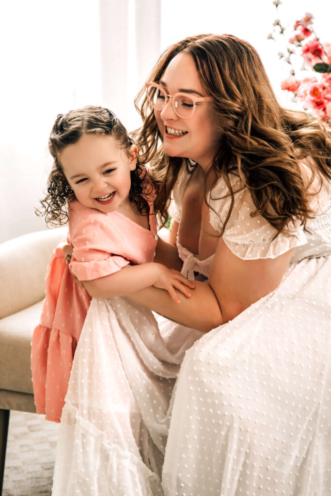 Joyful moment of a mother and daughter in pink and neutral spring photoshoot outfits, giggling together during a Spring Blush Mother’s Day photoshoot session.