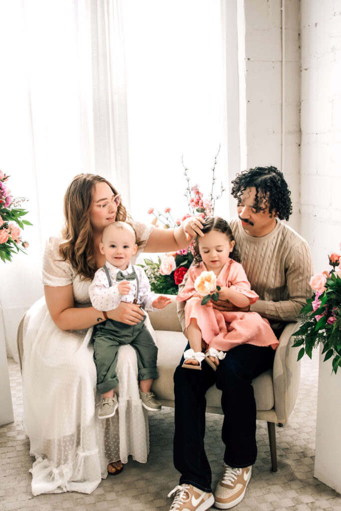 Family wearing pink and green spring photoshoot outfits in a cozy, neutral-toned studio session.